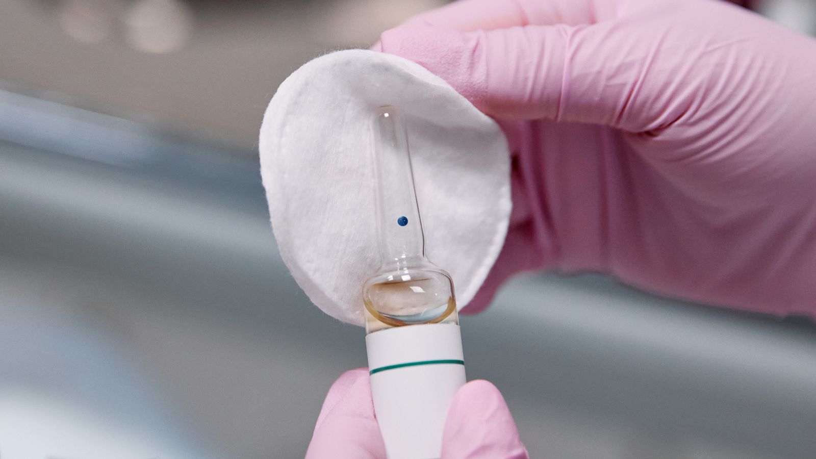 Close-up of gloved hands holding a small glass ampoule against a cotton pad.