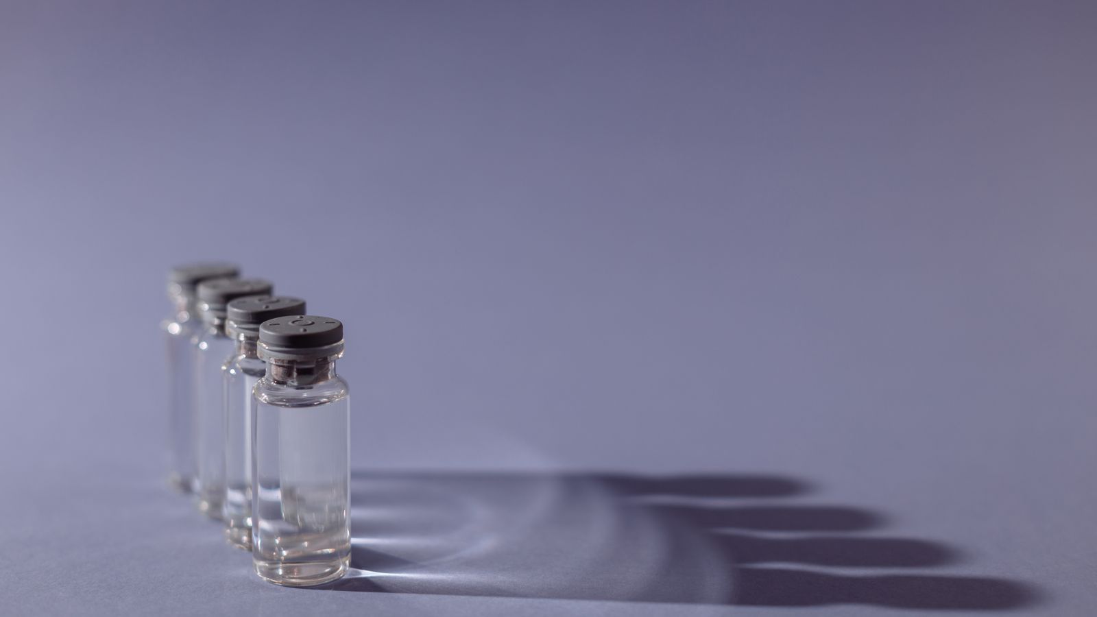 Close-up of small glass vials lined up in a row, each casting a long shadow.