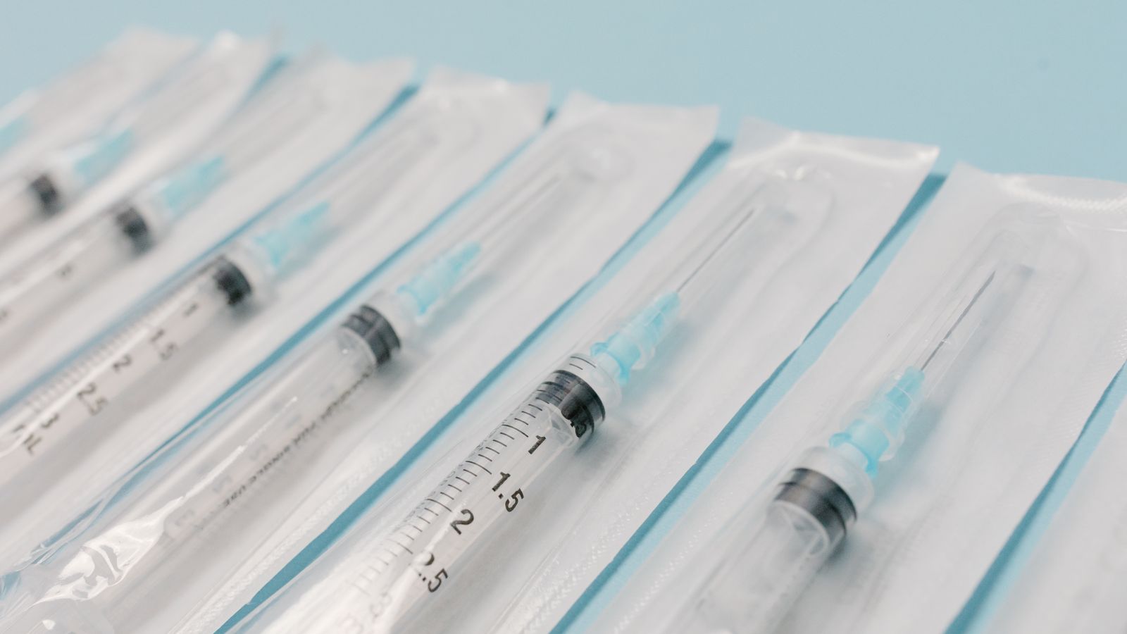 Close-up of several sterile syringes aligned in a row on a light blue surface.