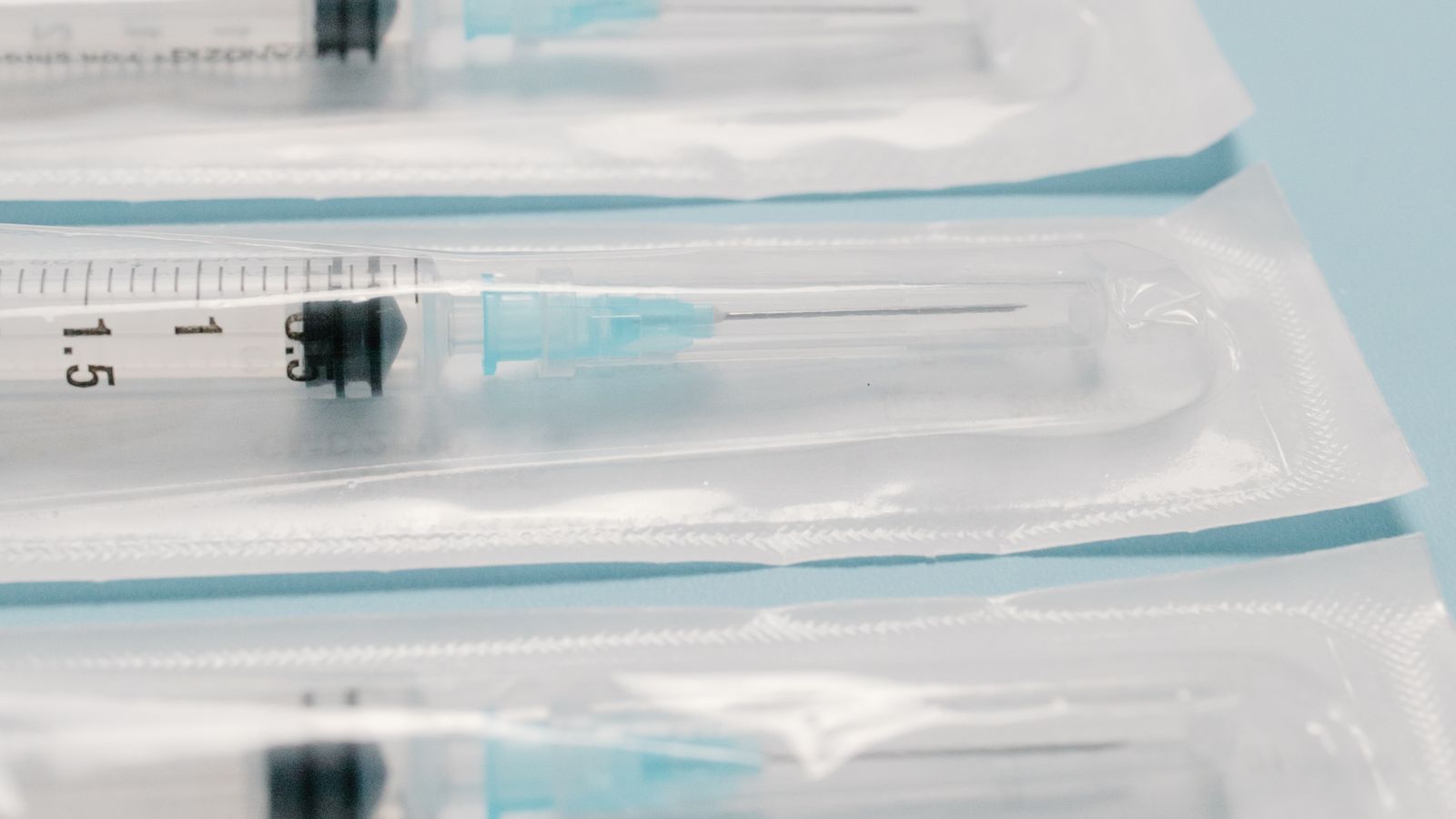 Rows of sterile syringes lined up in neat parallel rows against a blue background.