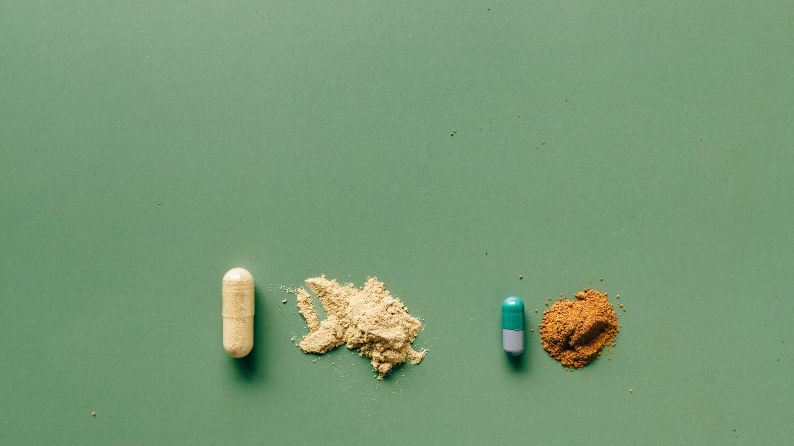 Variety of capsules and powders arranged on a green backdrop, showing different textures and container types.
